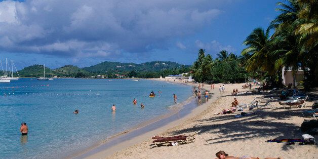 WEST INDIES St Lucia Reduit Beach Sunbathers and swimmers on sandy beach lined with palm trees. Yachts seen on the water and green hills behind