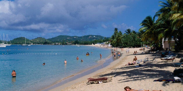 WEST INDIES St Lucia Reduit Beach Sunbathers and swimmers on sandy beach lined with palm trees. Yachts seen on the water and green hills behind