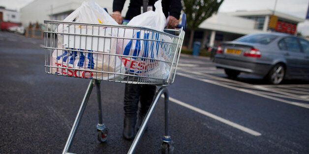 A customer pushes a shopping cart loaded with Tesco Plc branded carrier bags as she leaves one of the company's stores in this arranged photograph in London, U.K., on Wednesday, Oct. 3, 2012. Tesco Plc, the U.K.'s largest retailer, reported the first profit drop in almost two decades after increasing investment to halt declining supermarket sales. Photographer: Simon Dawson/Bloomberg via Getty Images