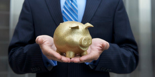 Businessman stands holding a golden piggy bank cradled in his hands