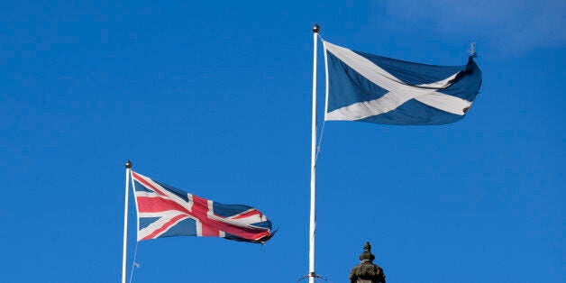 Scottish Flag (the Saltire or Cross of St. Andrew) and the British flag (the Union Jack) blowing together against a blue sky.