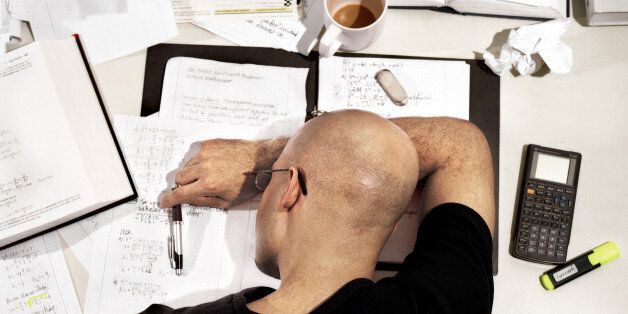 Young man with head down on desk covered in text books and paperwork