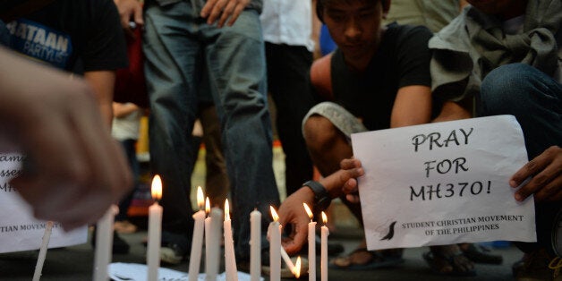 Students light candles as they hold placards in solidarity with families of the passengers of the missing Malaysia Airlines flight MH370 plane during a candle light vigil at the university belt in Manila on March 13, 2014. Malaysia said on March 13 that satellite images of suspected debris from a missing jet were yet another false lead, and debunked a report the plane had flown on for hours after losing contact -- leaving the nearly week-old mystery no closer to being solved. AFP PHOTO/TED ALJIBE (Photo credit should read TED ALJIBE/AFP/Getty Images)