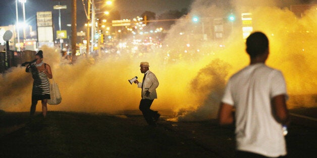 FERGUSON, MO - AUGUST 17: People make their way through the haze as tears gas fills the street during a demonstration over the killing of teenager Michael Brown by a Ferguson police officer on August 17, 2014 in Ferguson, Missouri. Despite the Brown family's continued call for peaceful demonstrations, violent protests have erupted nearly every night in Ferguson since his death. (Photo by Scott Olson/Getty Images)