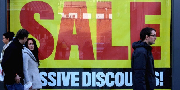 BRISTOL, ENGLAND - DECEMBER 22: Christmas shoppers pass sale signs displayed in a shop window as they look for last minute bargains on the high street on December 22, 2013 in Bristol, England. Although many retailers are already having sales, tomorrow is being predicted to be the busiest day in British retail history with some retail analysts predicting consumers will spend almost 4 billion GDP over 24 hours in a last-minute surge of present-buying. (Photo by Matt Cardy/Getty Images)