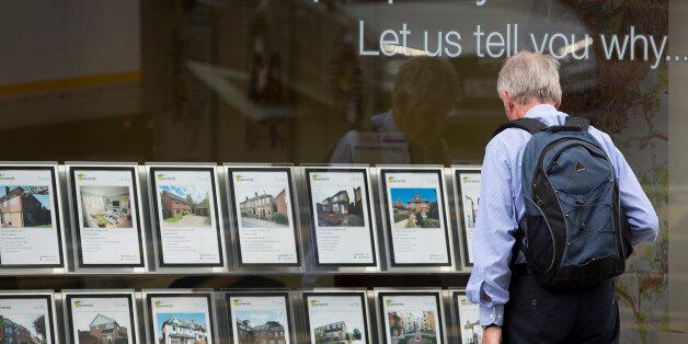 A pedestrian stands beneath a 'Your Property is HOT!' sign as he looks at information leaflets of residential properties displayed for sale in the window of an estate agents in Guildford, U.K., on Monday, June 23, 2014. As Britons brace for the Bank of England to announce steps to restrain the housing market this week, Chief Secretary to the Treasury Danny Alexander dismissed talk of a bubble. Photographer: Jason Alden/Bloomberg via Getty Images
