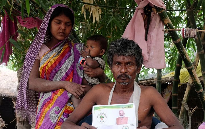 Nand Lal Mandhji, holds a letter about the Ayushman Bharat Medical Scheme, known as 'Modicare' as he sits outside his home with his family in Marwan village in Bihar.