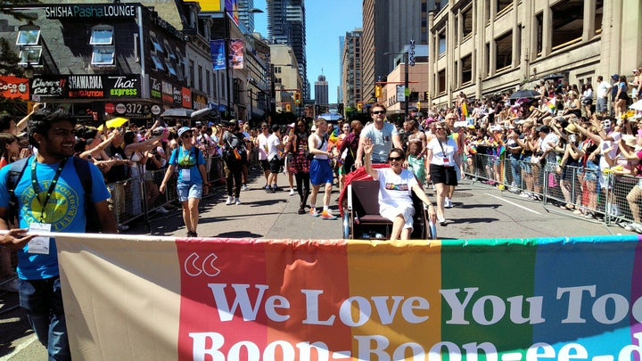 Sharon Hampson of Sharon and Bram sits in a rickshaw behind a banner at Toronto's Pride Parade on Sunday.