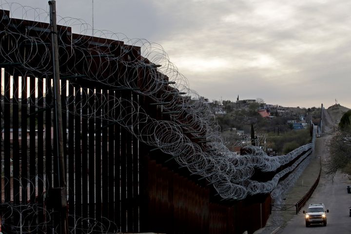 A U.S. Customs and Border Protection agent patrols on the U.S. side of a razor-wire-covered border barrier that separates Nogales, Mexico, from Nogales, Arizona.