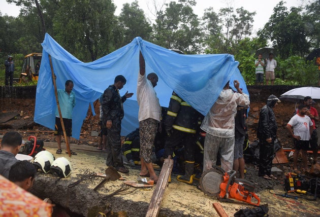 Rescue workers shelter from rain with a plastic sheet as they attempt to bring out a child found alive under the debris at the site of a wall collapse in Mumbai on July 2, 2019