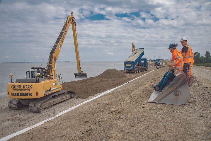 Workers dump sand mixed with gravel, a foundation for asphalt, on a sea dike.