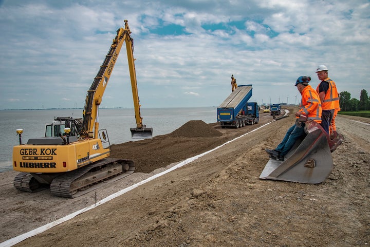 <em>Workers dump sand mixed with gravel, a foundation for asphalt, on a sea dike.</em>