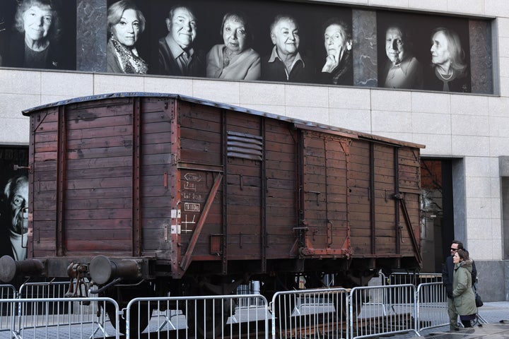 Portraits of Holocaust survivors are displayed in April 2019 at New York's Museum of Jewish Heritage, as a vintage German train car, like those used to transport people to Auschwitz and other Nazi death camps, is seen in front of the building.