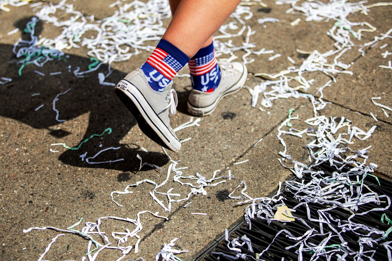 A person walks along the parade route as ticker tape litters the ground. 
