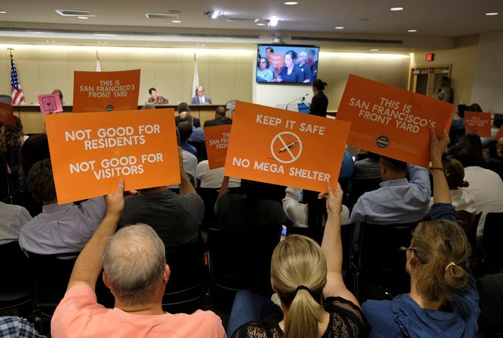 People opposed to a proposed homeless shelter hold up signs during a meeting of the Port Commission, April 23, 2019, in San Francisco.