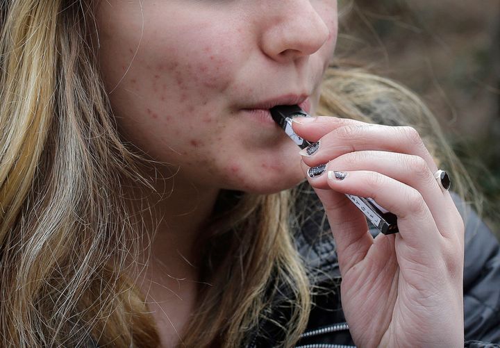 A 15-year-old high school student uses a vaping device near her school in Cambridge, Mass.