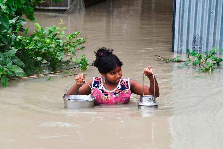 A girl carries drinking water as she wades through flood waters at Pabhokathi village in Morigaon district of Assam on July 15, 2019. 