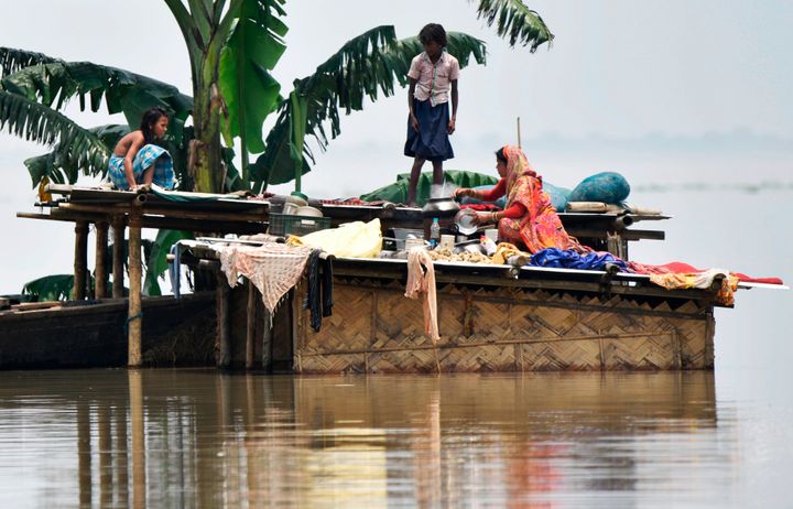 Members of a family stand atop a hut at the flood-affected area of Hatishila in Kamrup district of Assam state on 16 July 2019. 