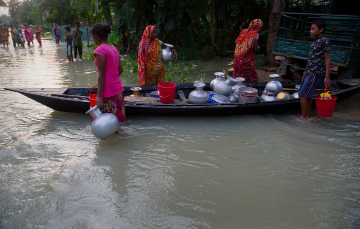 Flood-affected villagers stand near a boat filled with vessels of drinking water in Jhargaon, east of Guwahati, Assam, on 17 July 2019.