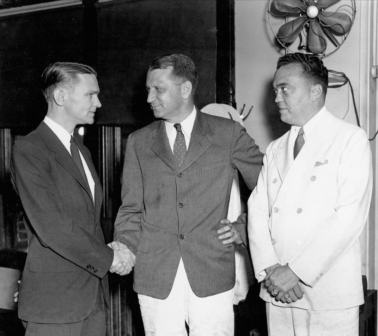  Με το άσπρο κουστούμι, ο αρχηγός του FBI, Τζέι Εντγκαρ Χούβερ. Αριστερά διακρίνεται ο Μέλβιν Πέρβις ενώ δέχεται συγχαρητήρια, από τον γενικό εισαγγελέα του Υπουργείου Δικαιοσύνης, Γουίλιαμ Στάνλεϊ. (26 Ιουλίου 1934)