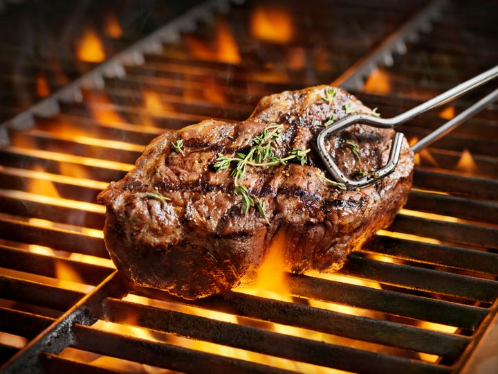 A sirloin steak with fresh thyme on top is prepared on a hot grill.