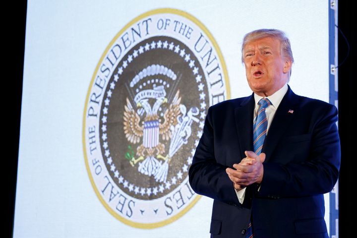 President Donald Trump speaks to a college Republican group as the doctored presidential seal showing Russian symbols and golf clubs is projected behind him.