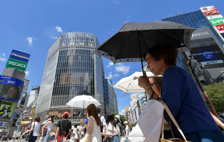 猛暑の中、日傘をさしながら街を歩く人々