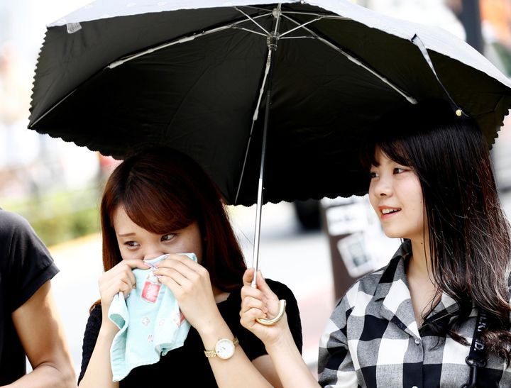 A woman wipes her face and another woman holds a parasol on the street during a heatwave in Tokyo, Japan