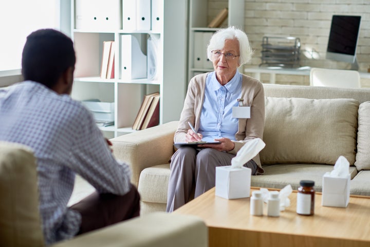 Serious senior female psychologist listening to patient and making notes for understanding problem in personal office