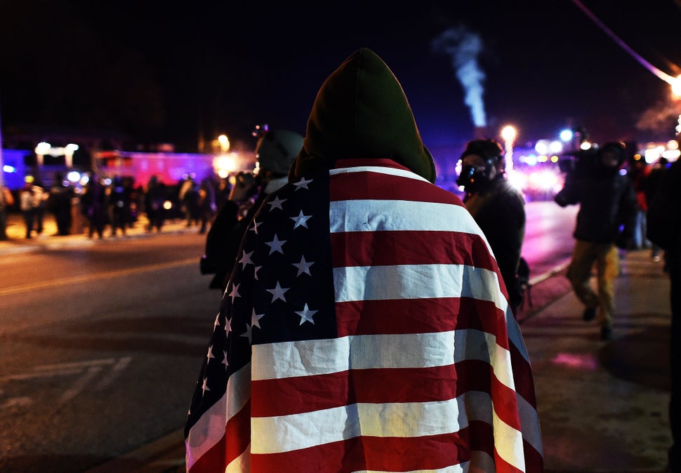 A protester wraps himself in a US flag in Ferguson, Missouri, on November 25, 2014 during demonstrations a day after violent protests and looting following the grand jury decision in the fatal shooting of a 18-year-old black teenager Michael Brown. Protest marches sprang up in cities across the US on November 25, amid a tense security operation in Ferguson, the Missouri town at the center of the country's latest racially-charged stand-off. Clashes erupted in the St Louis suburb for a second night, after grand jury's decision not to prosecute a white police officer for shooting dead an unarmed black teenager. AFP PHOTO/Jewel Samad (Photo credit should read JEWEL SAMAD/AFP/Getty Images)