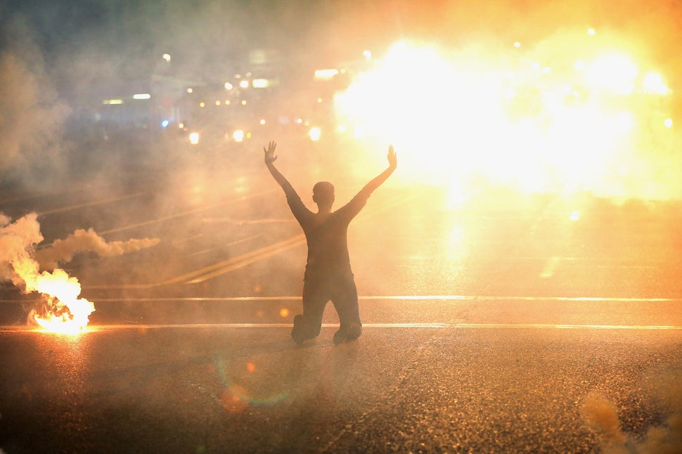 FERGUSON, MO - AUGUST 17: Tear gas reigns down on a woman kneeling in the street with her hands in the air after a demonstration over the killing of teenager Michael Brown by a Ferguson police officer on August 17, 2014 in Ferguson, Missouri. Despite the Brown family's continued call for peaceful demonstrations, violent protests have erupted nearly every night in Ferguson since his August 9, death. (Photo by Scott Olson/Getty Images)