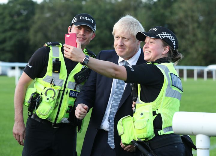 Prime Minister Boris Johnson has a selfie with police officers as he arrives to meet emergency crews during a visit to Whaley Bridge Football Club in Derbyshire.