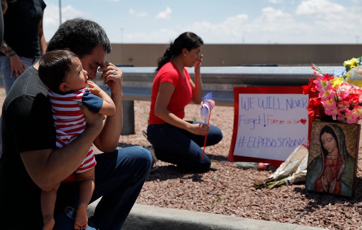 Dr. Julio Novoa, left, and Danielle Novoa, right, kneel beside a makeshift memorial with their 10-month-old son Richard Novoa at the scene of a mass shooting at a shopping complex Sunday, Aug. 4, 2019, in El Paso, Texas.