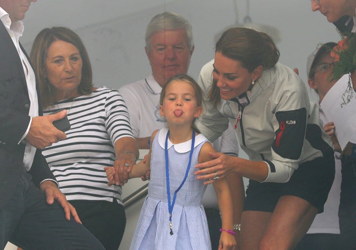 Princess Charlotte, flanked by her grandmother and mother, gestures through a window at the prize giving after the King's Cup