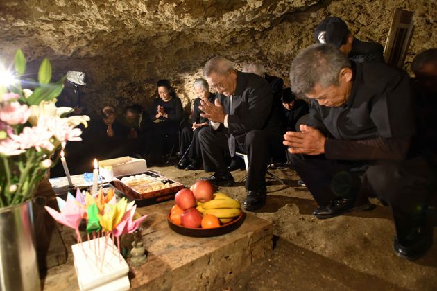 チビチリガマの中で手を合わせる遺族ら（2018年、沖縄県読谷村）