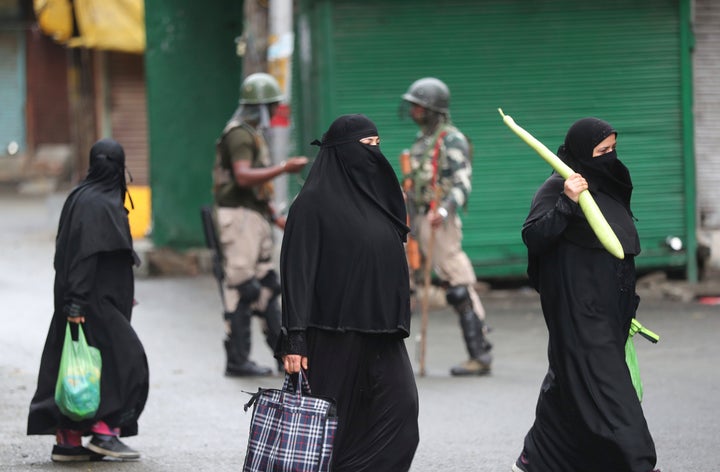 Kashmiri women holds bags filled with essentials and walk past Indian paramilitary soldiers closing off a street in Srinagar on Aug. 10, 2019. 