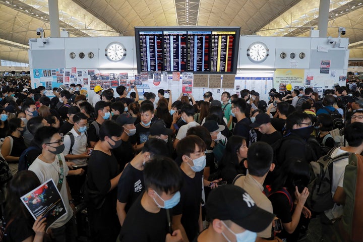 Protesters gather near a flights information board during a protest at the Hong Kong International Airport, Monday, Aug. 12, 2019.