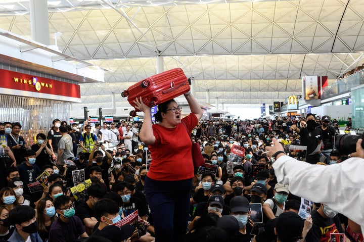 A traveller (C) shouts while holding her luggage as she tries to enter the departures gate area at Hong Kong's international