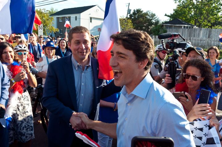 Prime Minister Justin Trudeau shakes hands with Conservative Leader Andrew Scheer while walking with the crowd during the Tintamarre in celebration of the National Acadian Day in Dieppe, N.B., on Aug. 15, 2019.