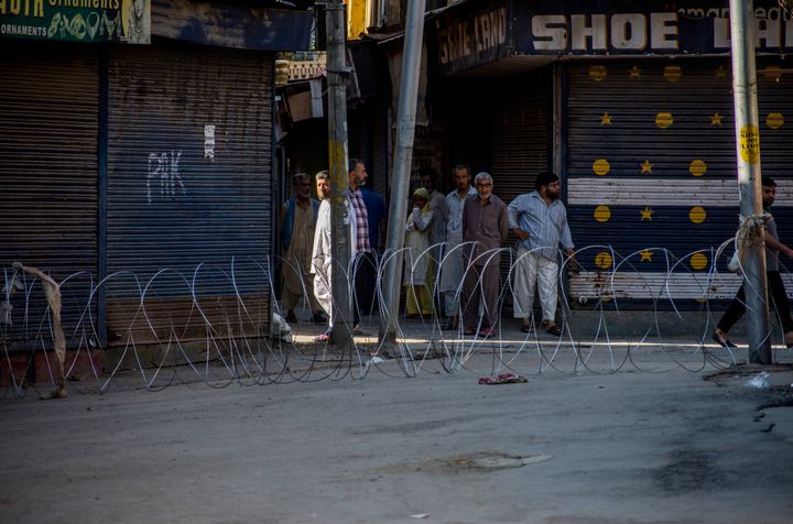 Kashmiris wait to cross through a concertina razor wire cordon as they look towards paramilitary troopers standing guard amid curfew-like restrictions in the Habba Kadal, on August 18, 2019 in Srinagar.