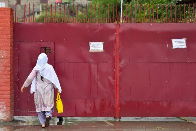 A Kashmiri woman speaks to a worker behind the door of a closed school in Srinagar on August 19,