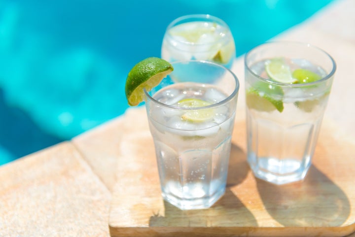 Colourful and vivid picture of a cold Gin and Tonic with fresh line and ice in sunshine by the pool