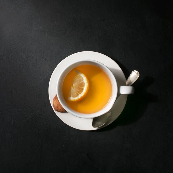 Overhead view of a white cup with lemon tea. Rustic moody black background.