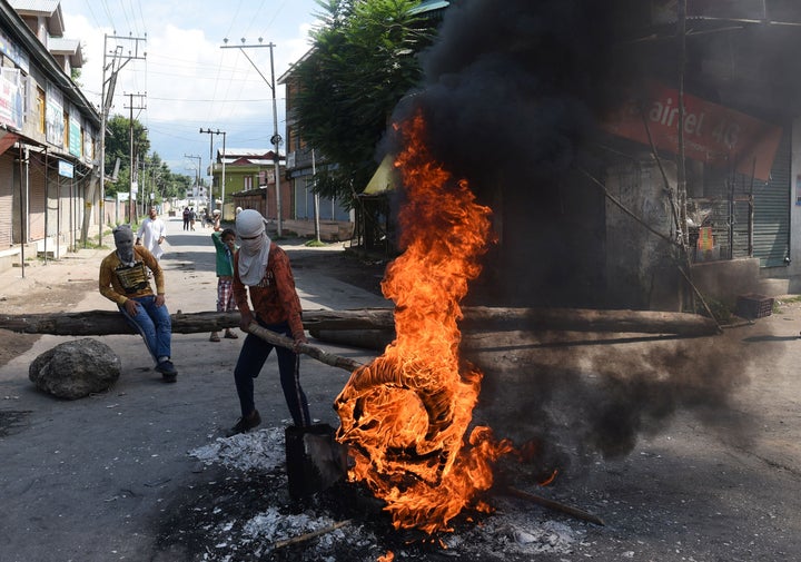 A protester holds a burning tyre near a barricade set by them to block the road during a protest against the abolishing of Article 370, on August 20, 2019 on the outskirts of Srinagar