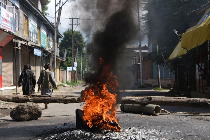 People walk past burning tires near a barricade during a protest against the abolishing of Article 370, on Aug. 20, 2019 in Srinagar, India.