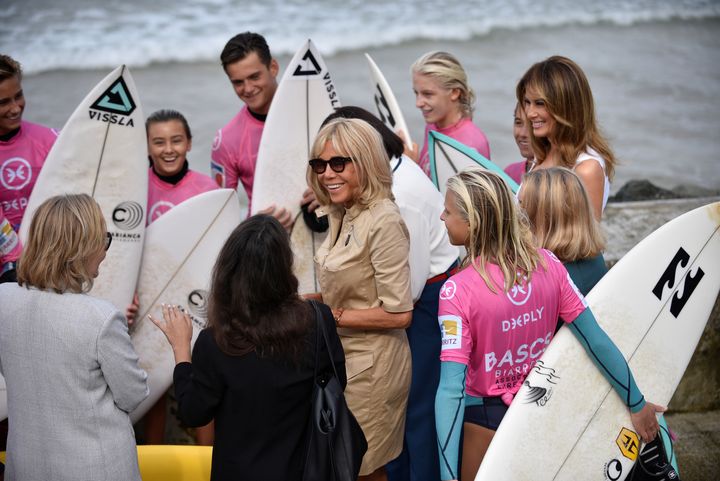 Κατενθουσιασμένες οι Μπριζίτ Μακρόν και Μελάνια Τραμπ συνομιλούν με νεαρούς σέρφερ στην παραλία.