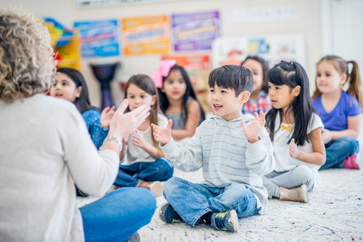 Group of kids sitting on the carpet in their kindergarten classroom.They are clapping along to music.