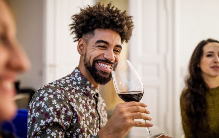 Smiling young man drinking red wine during dinner party at home