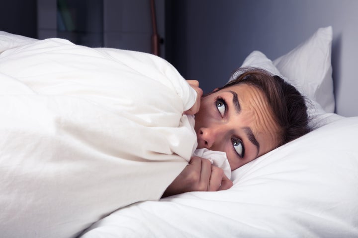 Scared Woman Pulling Bed Sheet Over Self On Bed At Night