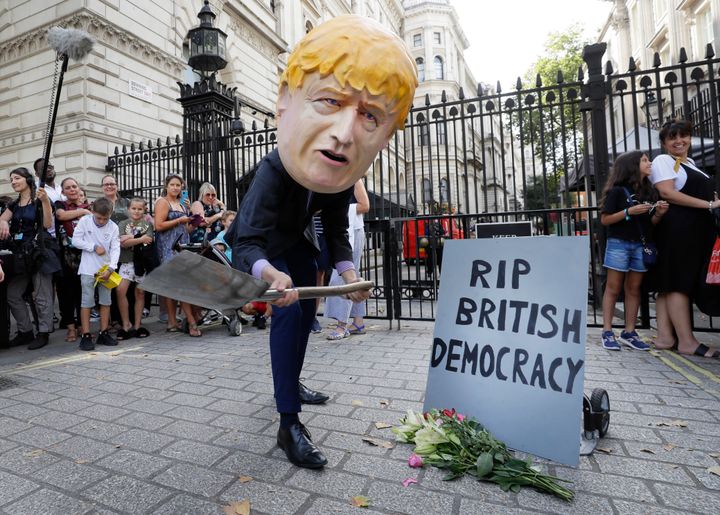 A man in a giant Boris Johnson 'head' digs a grave at the foot of a pretend tombstone outside Downing Street in London, Wednesday, Aug. 28, 2019. Britain's Queen Elizabeth II has approved the U.K. government's request to suspend Parliament amid a growing crisis over Brexit. Prime Minister Boris Johnson spoke to the queen on Wednesday to request an end to the current Parliament session in September.(AP Photo/Kirsty Wigglesworth)